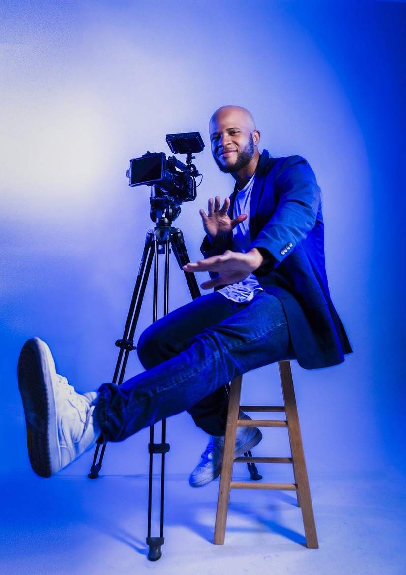 Aaron Daniels seated beside a cinema camera in blue studio light