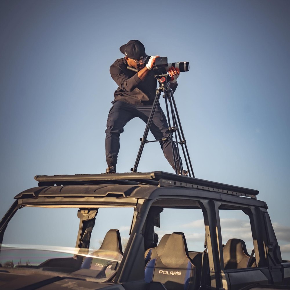Aaron filming from the roof of a Polaris off-road vehicle against a clear sky