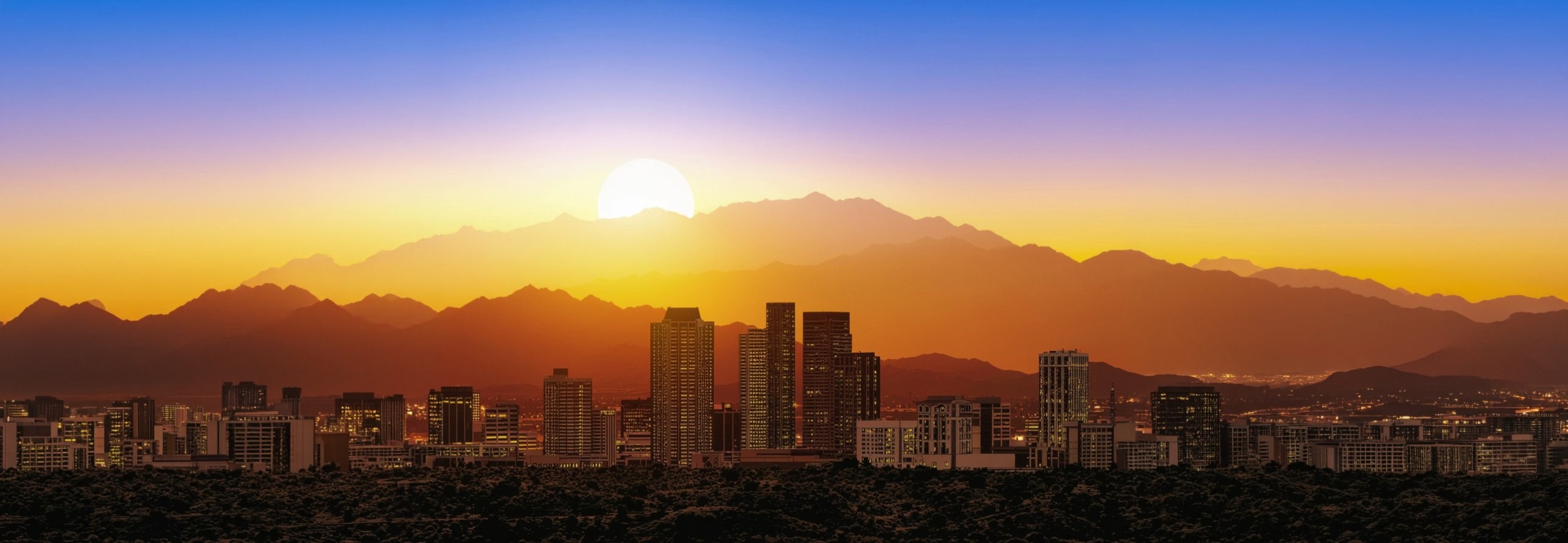 Downtown Phoenix skyline at sunset, the sun setting over layered desert mountains