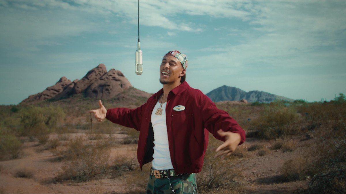 EA Jones performing at one hanging mic in the open desert, red rock buttes behind him